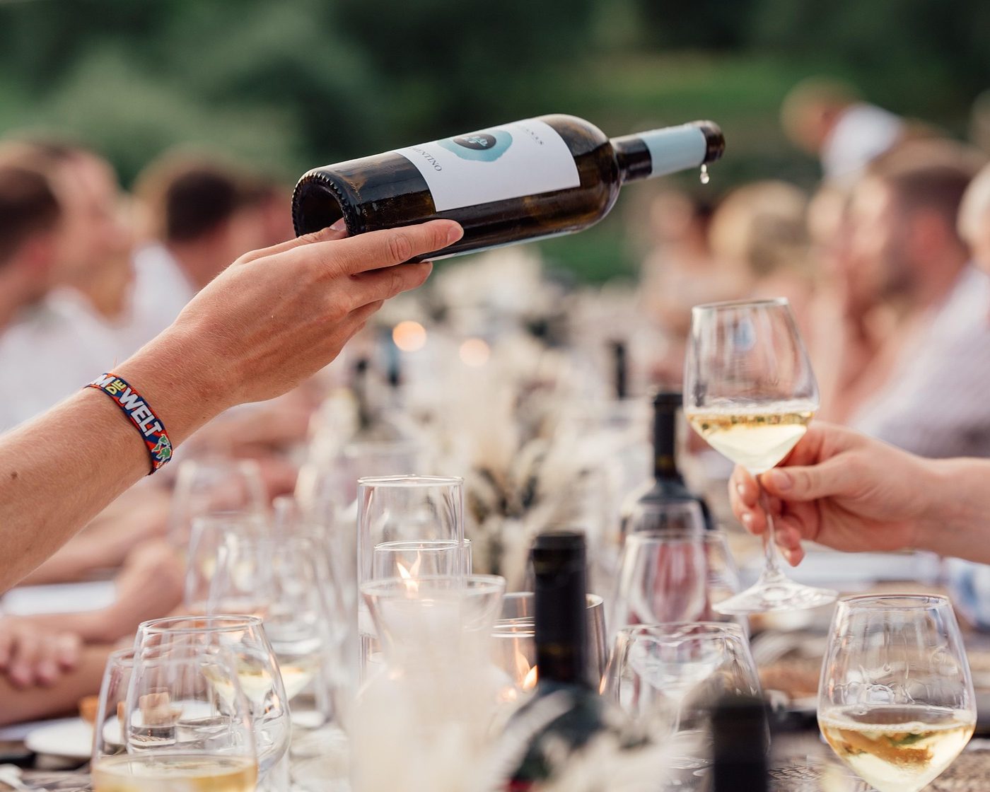 Eine Hand schenkt Weißwein an einer gedeckten Tafel im Freien ein