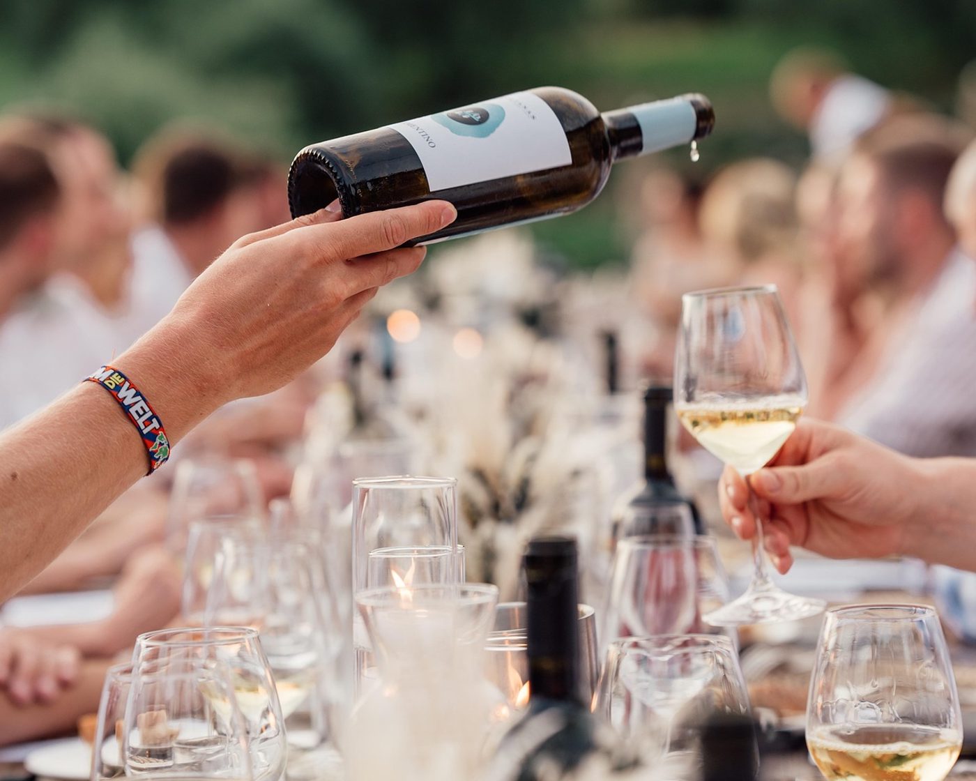 Eine Hand schenkt Weißwein an einer gedeckten Tafel im Freien ein