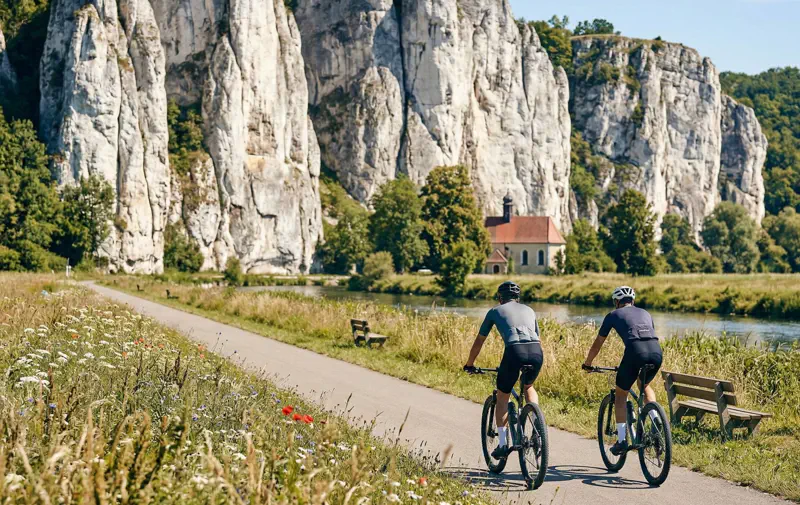 Fahrradfahrer vor riesigen weißen Jurafelsen im Altmühltal auf flachem Asphalt