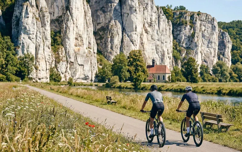 Fahrradfahrer vor riesigen weißen Jurafelsen im Altmühltal auf flachem Asphalt